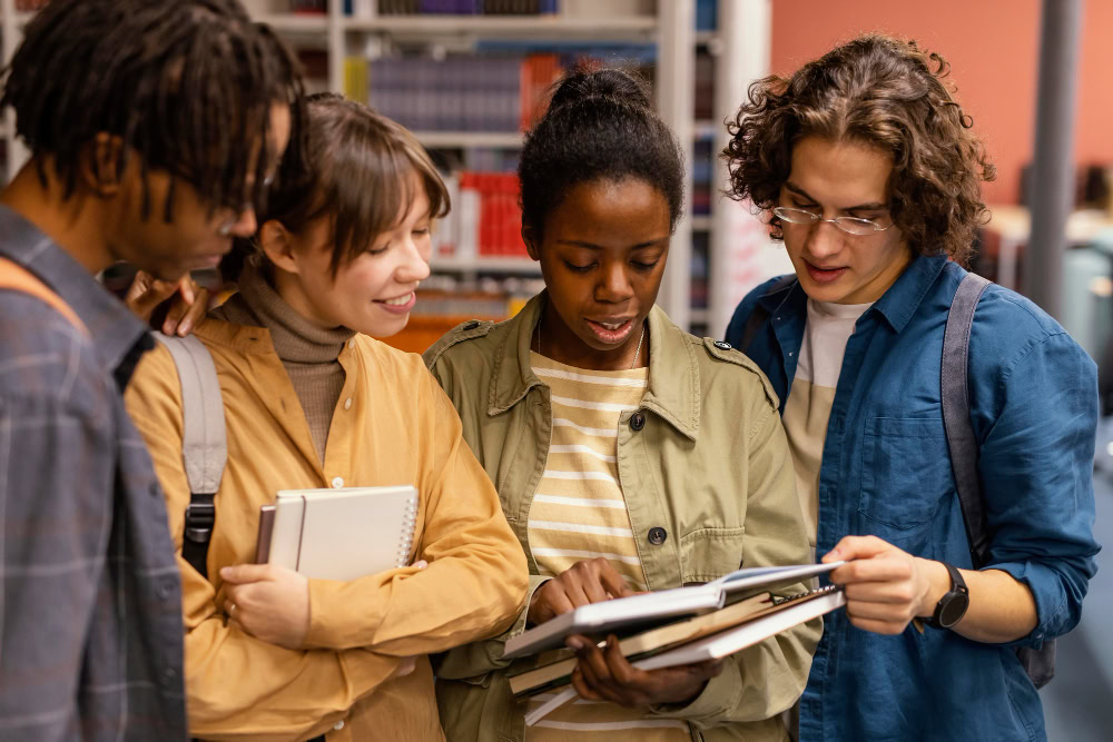 A group of young adult college students are standing next to each other reading from a book