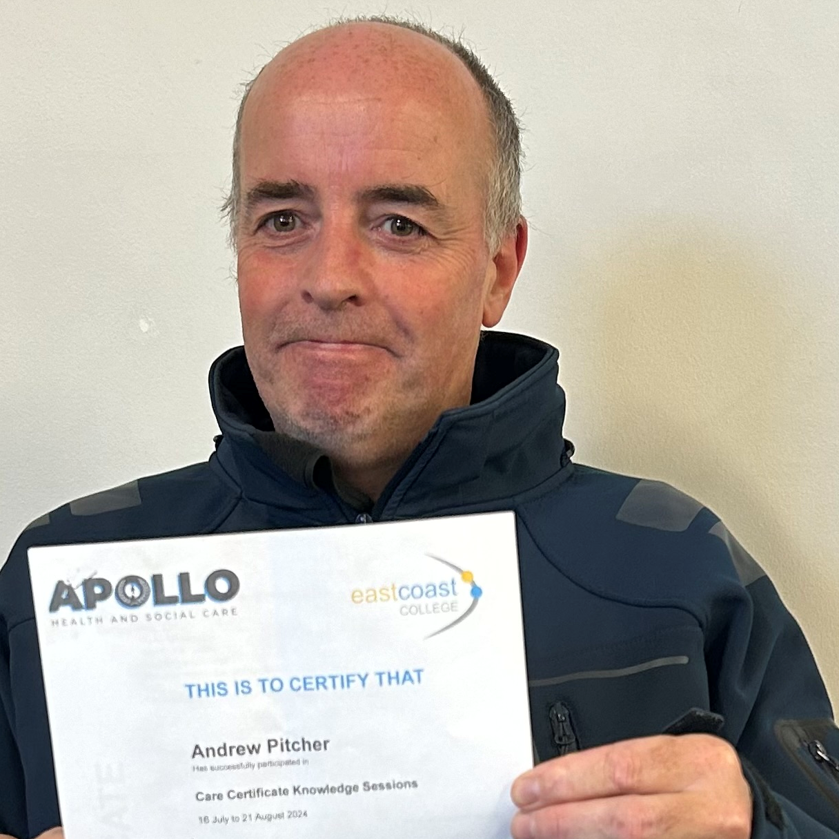 A bald middle-aged man is happily looking at the camera holding his Care Certificate.